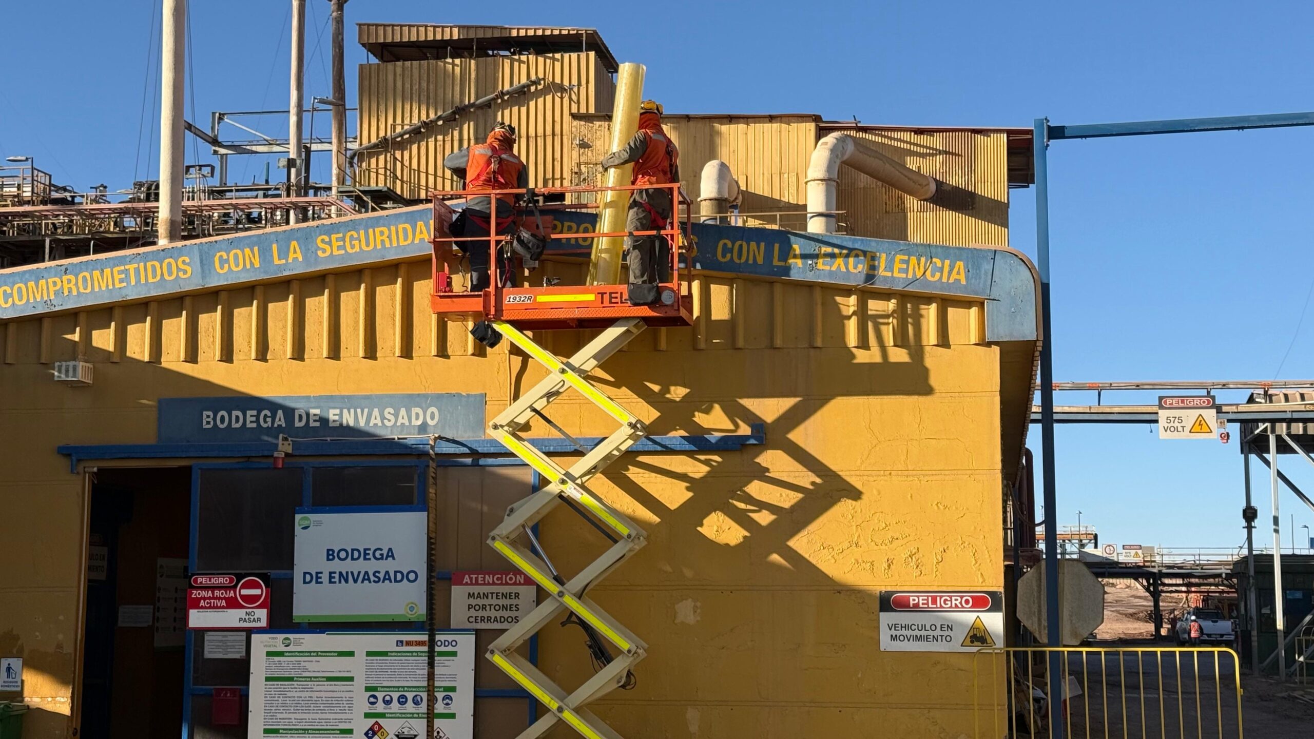 Equipo en tijera elevadora trabajando en fachada de planta industrial